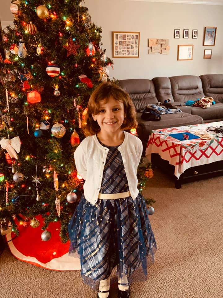 Holley in her pretty new Christmas dress by the tree.