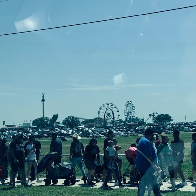 A line of people waiting to get in the festival gates along with some of the carnival in the back.