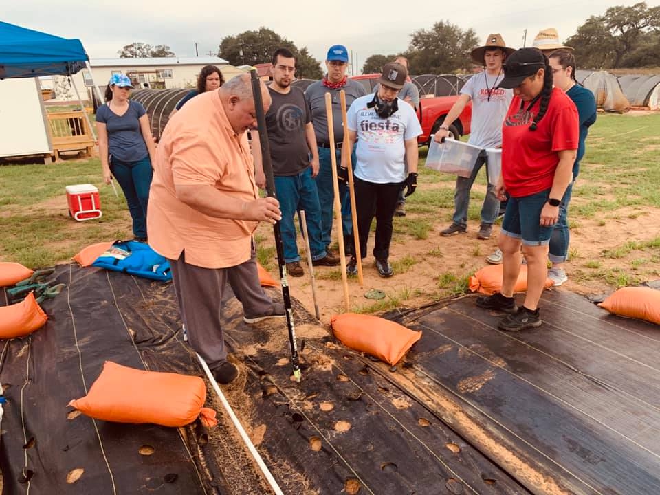 David demonstrates how to cover the corn seeds with dirt without having to bend over, using the end of a stick.