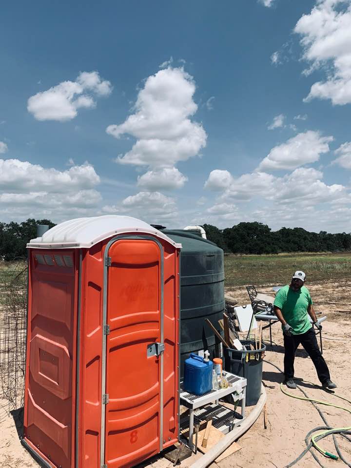 Our orange outhouse is next to our green water tank. Water tank is being filled in photo.