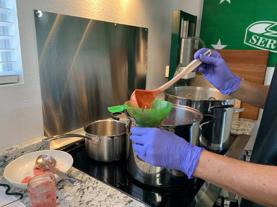 Here, DaLaina ladels some more strawberry jam into a glass jar.
